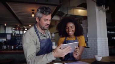 Hevesli kafe çalışanları, son moda kafede elinde kahveyle ayakta duran tabletle karar verirken sohbet ediyorlar..
