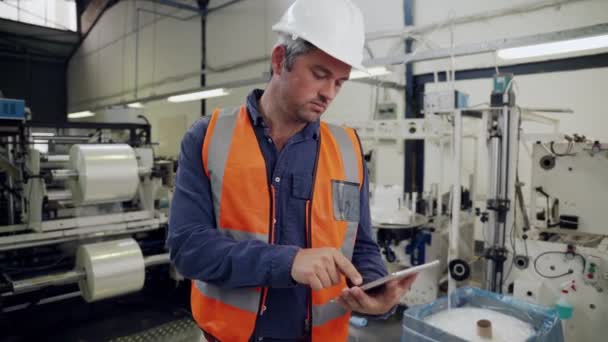 Hombre de negocios hombre de desplazamiento a través de correos electrónicos en tableta digital charlando con el gerente de pie en la fábrica — Vídeos de Stock