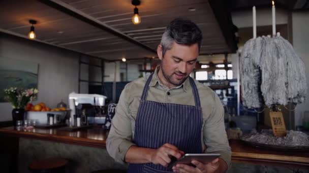 Guapo dueño de la cafetería masculina desplazándose en la tableta, mientras que de pie en el interior de la cafetería elegante. — Vídeo de stock