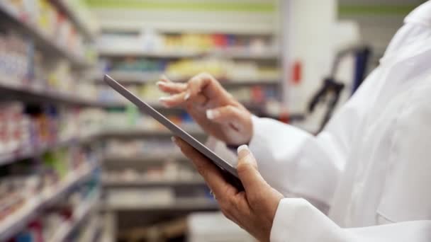 Крупним планом жіночий фармацевт прокручує рецепти на цифровому планшеті, що стоїть у білому пальто в чистій аптеці — стокове відео