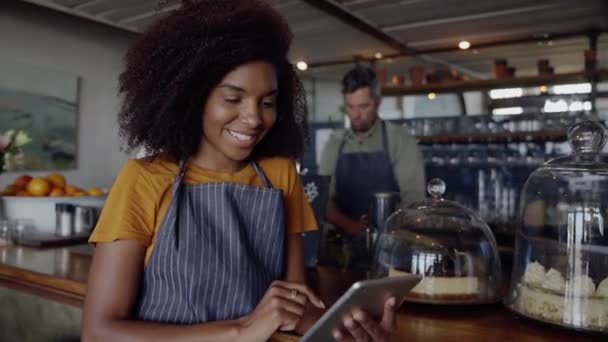 Afroamerykanin właściciel przewijania na tablecie, opierając się na liczniku obok pysznych ciast w modnej kawiarni. — Wideo stockowe