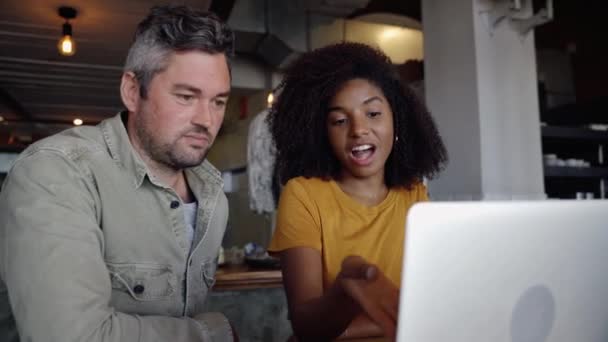 Compañeros de trabajo masculinos y femeninos discutiendo información importante sobre el portátil digital sentado en la cafetería de moda. — Vídeo de stock