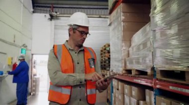 Kafkasyalı işadamı, depo fabrikasındaki adada yürüyen dijital tablet üzerindeki paketlerin listesini kontrol ediyor.