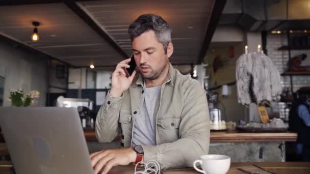 Mężczyzna na telefon służbowy z kolegą organizującym finanse na laptopie podczas sączenia kawy w funky kawiarni — Wideo stockowe