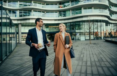 İki meslektaş, sıcak kahvenin tadını çıkarırken iş yerinde toplantıları tartışıyorlar.