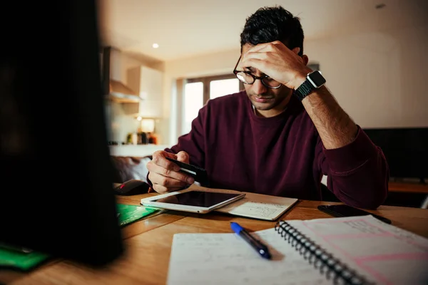 Stresli karışık ırk işadamı çevrimiçi ödemeler yapmaya çalışıyor. Kredi kartı tutuyor ve dijital tablette arama yapıyor. 