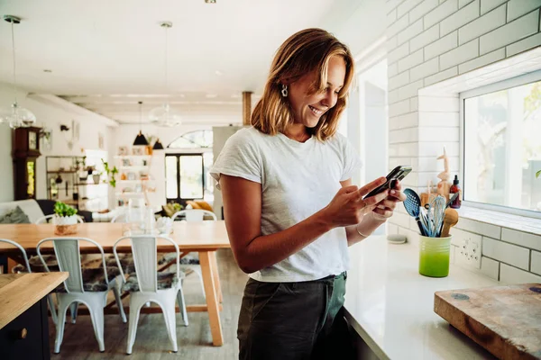 Studentessa caucasica che lavora da casa digitando su un dispositivo cellulare in piedi in cucina — Foto Stock