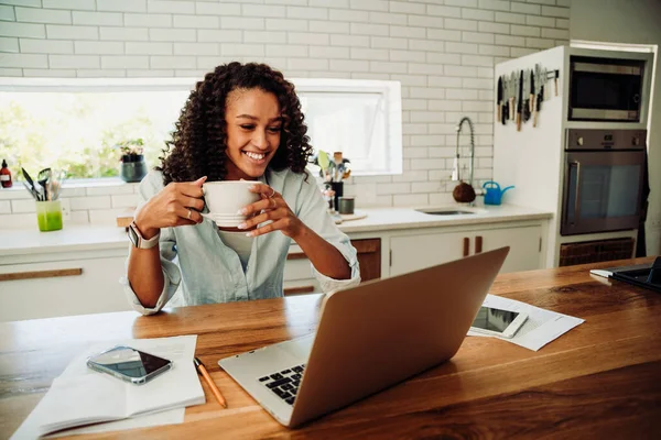 Razza mista sorridente studentessa in possesso di caffè caldo sorridente mentre in videochiamata con gli amici sul computer portatile — Foto Stock