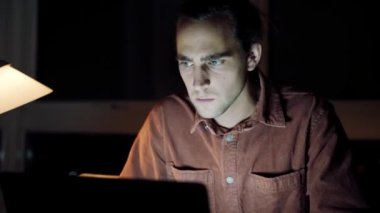 Caucasian male free lance photographer working late at night typing on laptop in home office