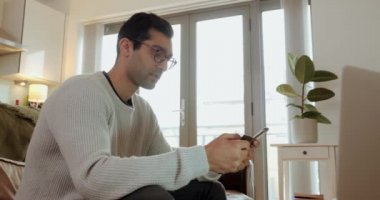Mixed race business man typing on cellular device while working from home sitting on couch