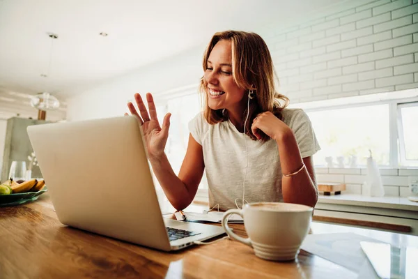 Studentessa caucasica in videochiamata con gli amici che digitano sul computer portatile sorseggiando caffè caldo che lavora in cucina — Foto Stock