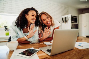 Melez yarış arkadaşları dizüstü bilgisayarda el sallarken mutfakta gülümsüyor.