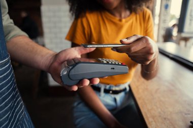 Afro-Amerikalı kadın, akıllı telefonlu kart makinesinin barkod kodunu tarıyor. Kahvenin parasını funky cafede ödüyor..