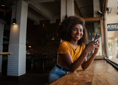 Güzel etnik kız arkadaşlarına akıllı telefondan mesaj atıyor kahve dükkanında dinleniyor.
