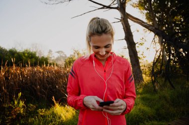 Güler yüzlü Kafkas atleti akıllı telefondan süzülüyor kulaklıkları dışarıda ormanda koşarken kulağında kulaklıklarla.