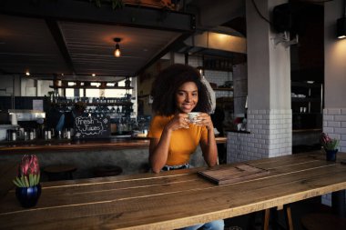 Gülümseyen Afrikalı kadın moda kafede oturmuş sıcak kahvenin tadını çıkarıyor. 