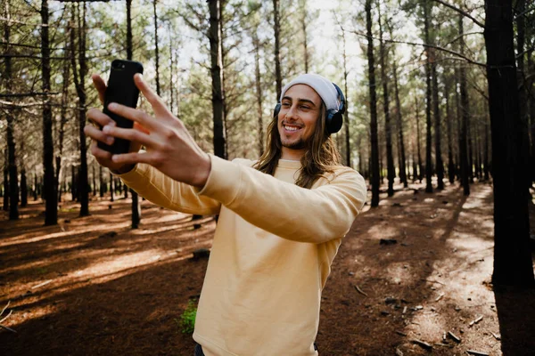 Caucasian male teen listening to music with earphones taking selfie while enjoying nature in woodlands — Stock Photo, Image