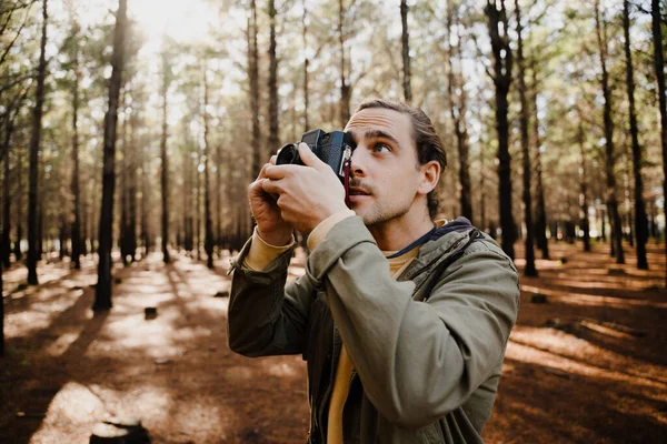 Jovem fotógrafo masculino na floresta tirando fotos com sua câmera de filme — Fotografia de Stock