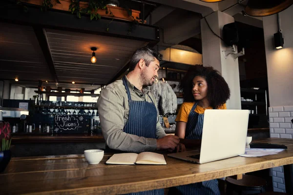 Maschio manager consigliare cameriera in grembiule dietro computer portatile e taccuino mentre in piedi in caffetteria alla moda. — Foto Stock