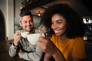 Gülümseyen mutlu melez çift modaya uygun kafede oturmuş sıcak espresso içiyor. 
