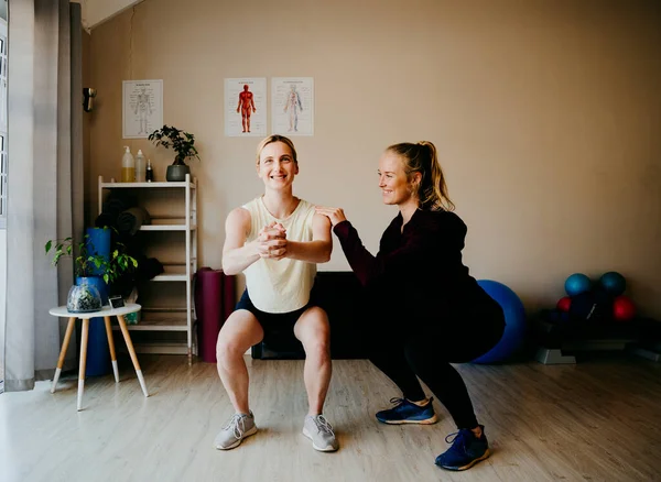 Patientin in Kniebeuge im Fitnessstudio, während Physiotherapeutin Gleichgewicht und Ausrichtung unterstützt — Stockfoto