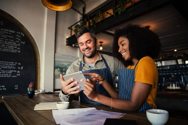 Manager e cameriera ridendo di disegni su tablet digitale in piedi con caffè caldo nel caffè — Foto Stock