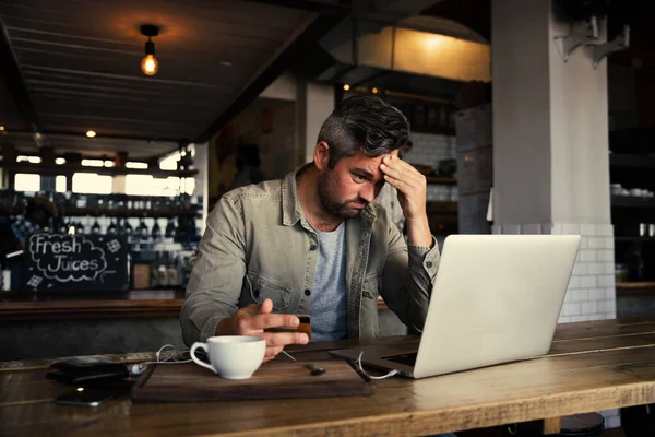 ストレスを感じるビジネスマンがヘッドとクレジットカードを持ち、ノートパソコンでホットコーヒーを飲む流行のカフェでオンライン決済を行う — ストック写真