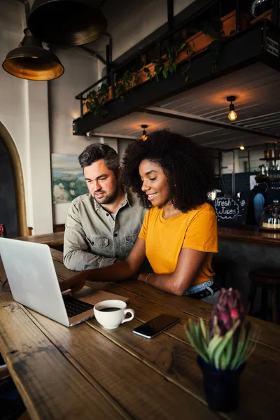 Sorridente multi gara coppia di navigazione sul computer portatile mentre beve caffè in negozio di caffè chic. — Foto Stock