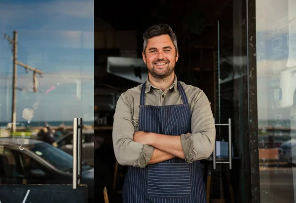 Kahvehanenin önünde duran gülümseyen beyaz erkek sahibi..