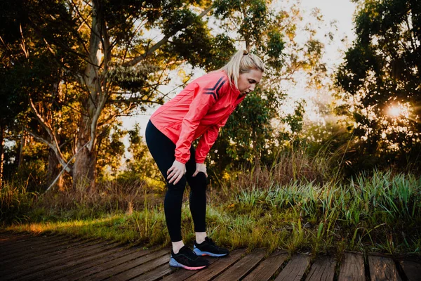 Mulher atlética cansada de correr no parque, dobrada sobre respirar pesadamente — Fotografia de Stock