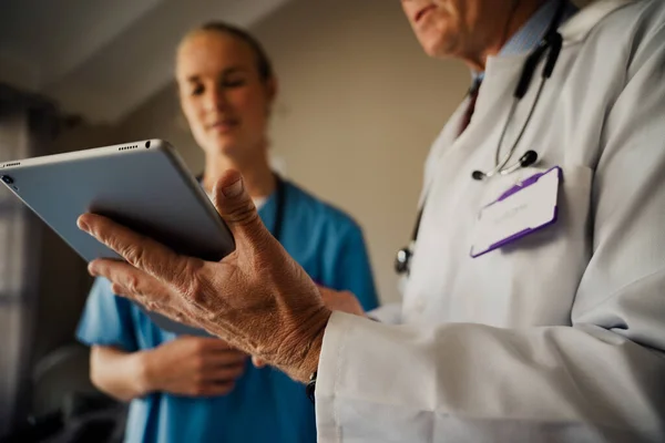 Gros plan du médecin masculin tenant une tablette numérique pendant que la stagiaire écoute les instructions debout dans un bureau organisé — Photo