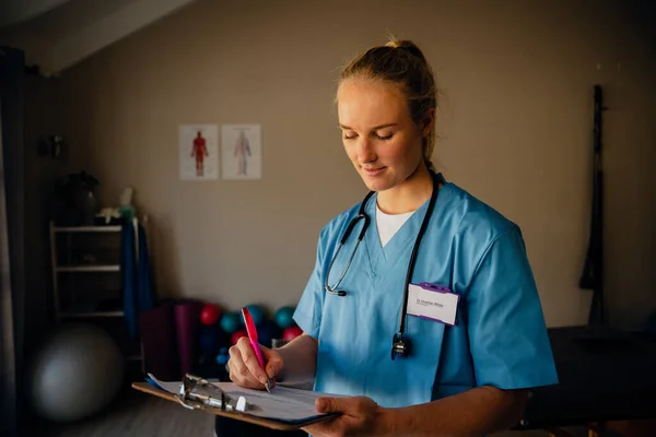 Portret van blanke vrouwelijke arts in scrubs met klembord en checklist — Stockfoto