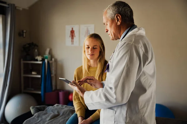 Mannelijke arts spreekt met vrouwelijke patiënten over bloed testresultaten zittend op uitklapbaar bed in modern kantoor. — Stockfoto