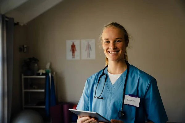 Close-up portret van jonge vrouwelijke arts met scrubs met tablet, glimlachen en gelukkig — Stockfoto