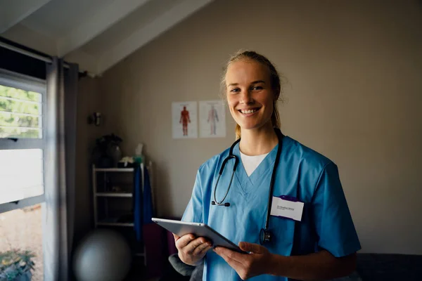 Πορτρέτο της νεαρής όμορφης Καυκάσιας γυναίκας γιατρού σε scrubs με ψηφιακή ταμπλέτα, χαμογελώντας — Φωτογραφία Αρχείου