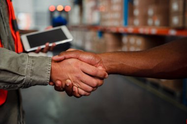 Close up of caucasian an ethnic male co-workers shaking hands after making successful deal in warehouse