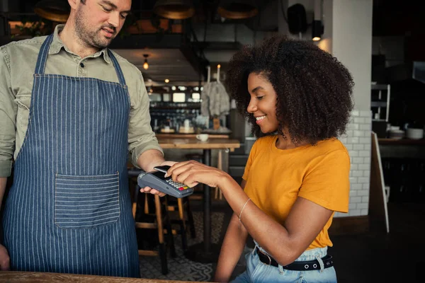 Afro-Amerikan kadın kredi kartı kullanıyor. Kahve için ödeme yapıyor. Moda kafede oturuyor..