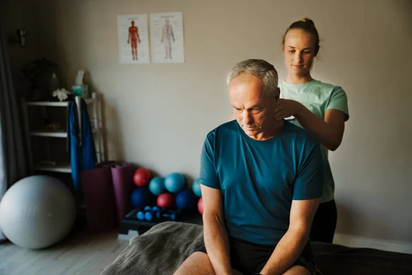 Woman therapist treating neck and back of elderly patient, diagnosis and recovery