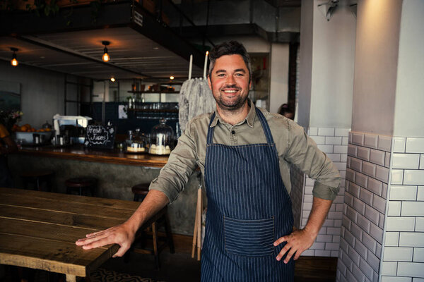 Good looking male coffee shop owner standing cheerfully in his coffee shop.