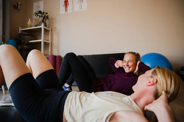 Smiling patient and physio-therapist practising crunching techniques for core stability practising in exercise studio