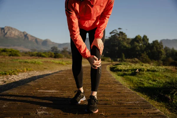 Καυκάσια γυναίκα με τραυματισμένο γόνατο ενώ τρέχει σε πίστα υπαίθριου πάρκου — Φωτογραφία Αρχείου
