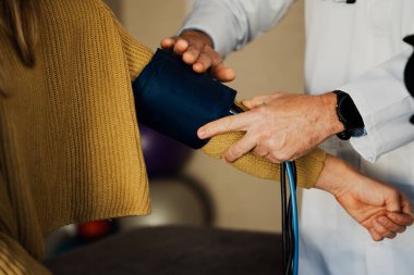 Male doctor removing blood pressure machine from female arm during checkup in doctors office.