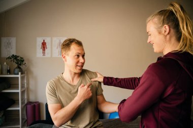Female physiotherapist stretching shoulder of male patient in pilates studio