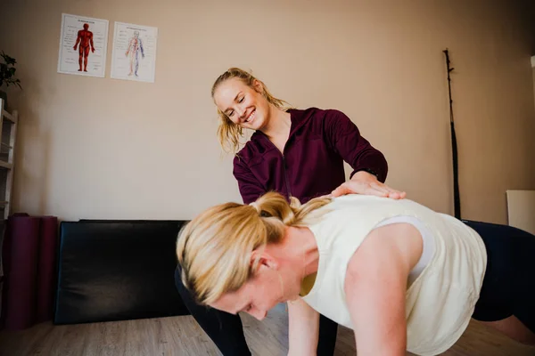 Female patient holding plank position while physio-therapist assists alignment and posture — Stockfoto