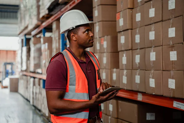 Concentrated factory worker holding digital tablet locating parcels for delivery standing in warehouse