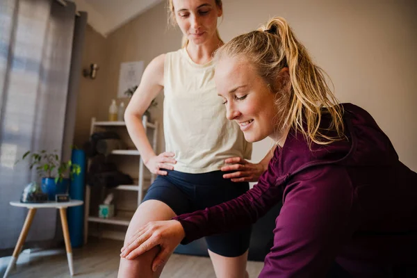 Physio-therapist assisting balance of patient while standing on one leg lifting knee to hip in exercise studio — Stockfoto