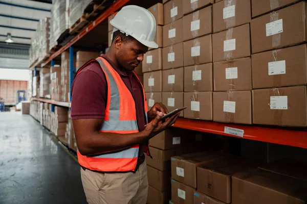 Male factory worker scrolling on digital device to find tracking process of parcels while standing in warehouse.