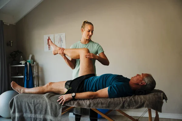 Female physiotherapist performs knee assessment for elderly man — Stockfoto