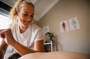 Physio-therapist massaging neck out injured patient lying on bed in rehab studio