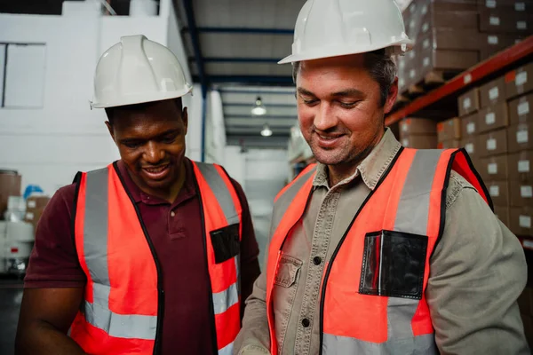 Smiling colleagues wearing overalls and hardhats laughing in factory